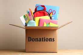 Box labeled donations filled with school supplies like books, pencils, and stationery